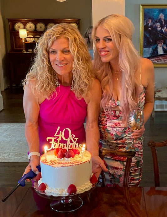 Two blonde women behind a birthday cake with a topper reading "40 and Fabulous."