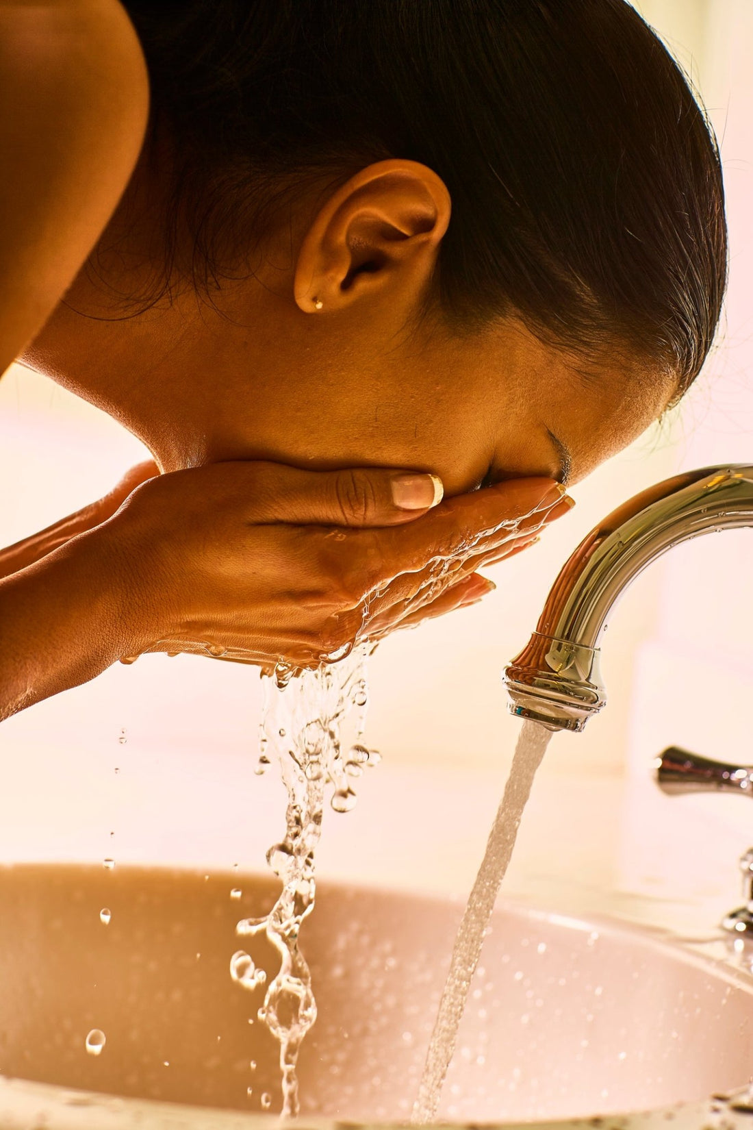 A woman over the sink splashing water onto her face.