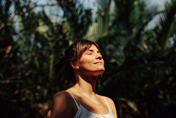 A woman smiling up at the sun with her eyes closed.