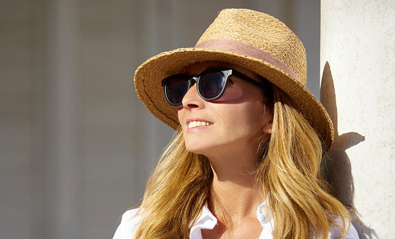 A woman in a hat and sunglasses smiling into the sun.