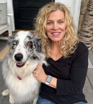 A woman smiling at the camera with a black and white dog at her side.