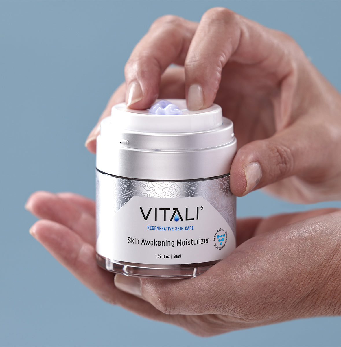 Close up of two hands holding a small tub of Vitali's skin awakening moisturizer.