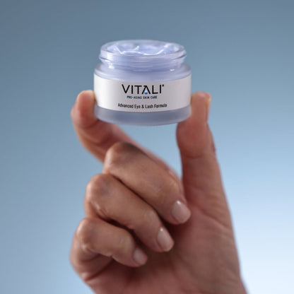 Close up of a hand holding a small tub of Vitali's blue advanced eye and lash formula.